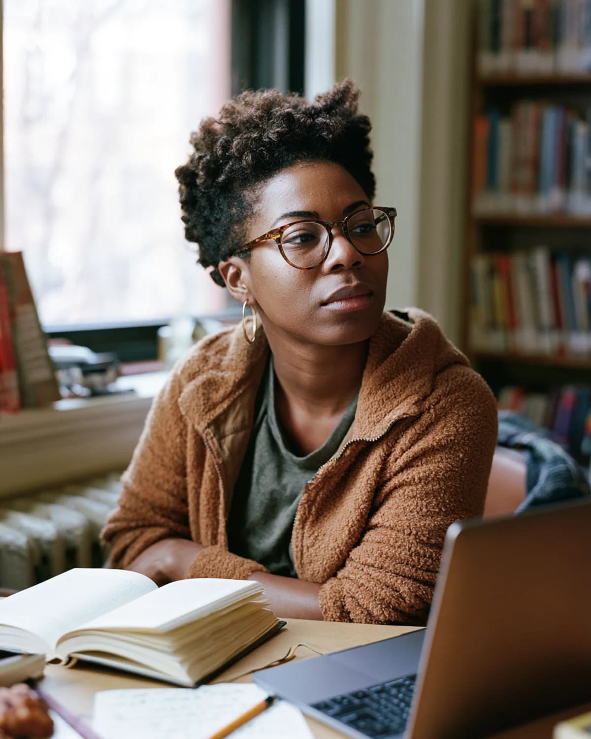 Black reader testing Kyndlore with an open book, laptop, and handwritten notes in a neighborhood library.