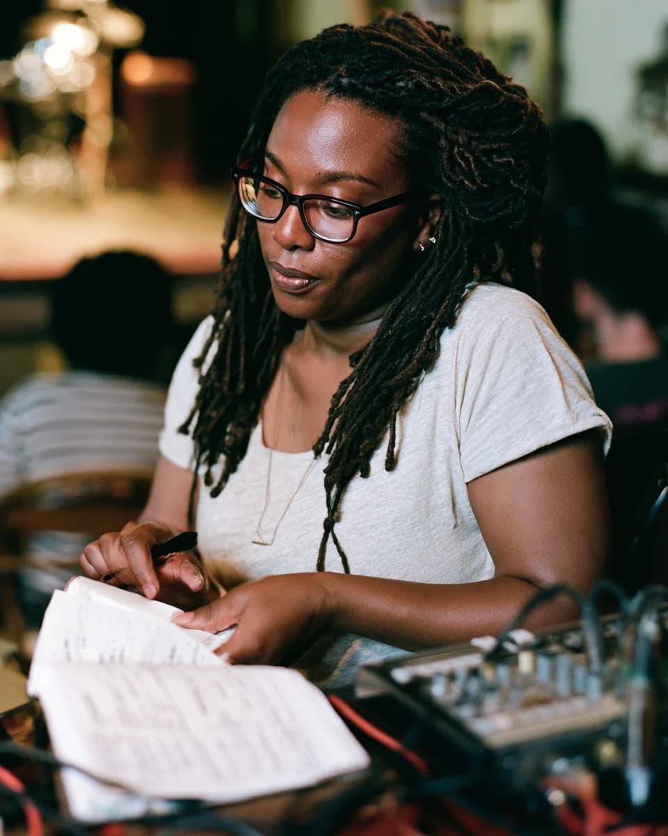 Black literary event producer preparing a live reading beside a compact sound desk.
